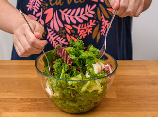Mieszać zieloną sałatę z dressingiem w szklanej salaterce - obrazy, fototapety, plakaty