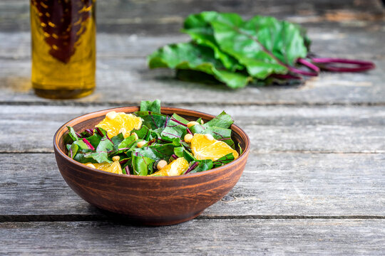 Salad of fresh chard and orange with pine nuts on a wooden table in a rustic style