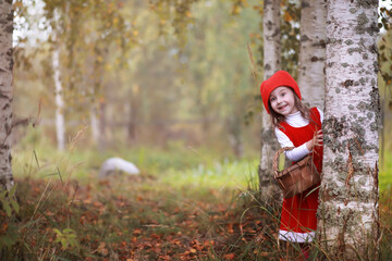 A little girl in a red hat and dresses is walking in the park. Cosplay for the fairytale hero "Little Red Riding Hood"