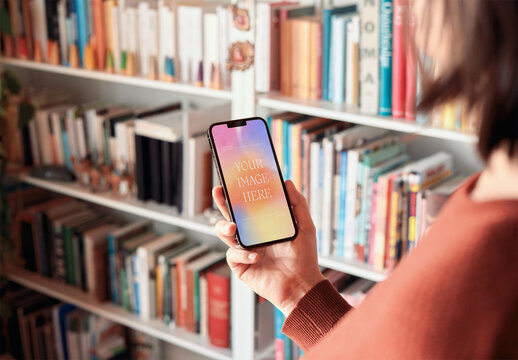 Mockup of woman holding smartphone with customizable screen by bookcase