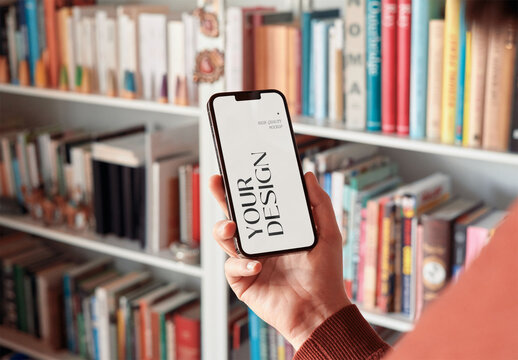 Mockup of woman holding smartphone with customizable screen by book shelf