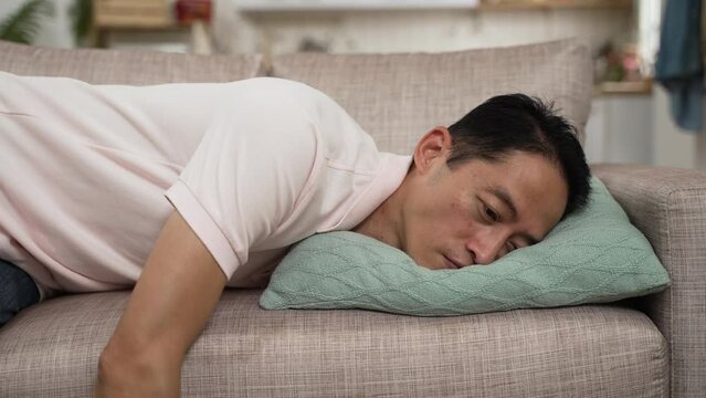 slow motion of depressed asian Korean mature mid age male falling lying on couch in a state of exhaustion in the living room at home. symptoms and problems of andropause in men concept