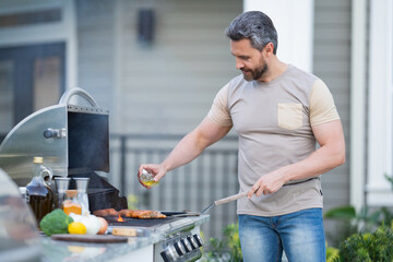 Barbecue concept. Middle aged hispanic man in t-shirt for barbecue. Roasting and grilling food. Roasting meat outdoors. Barbecue and grill. Cooking meat in backyard.