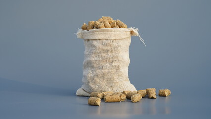 Burlap or jute bag of granulated chicken feed isolated on gray background. Closeup of poultry feed...