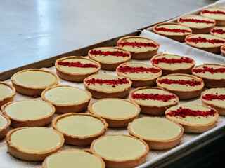 Mini-tarts with pistachio cream in the process of decorating with dry berries, close-up. Beautiful dessert