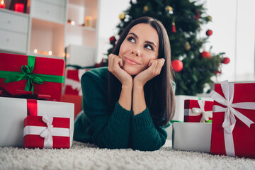 Photo of dreamy pretty lady dressed knitted x-mas sweater thinking lying floor arms cheeks indoors house room