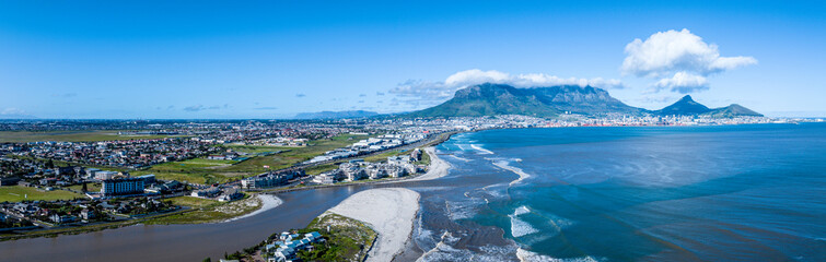 Panoramic view of the flooded Diep River flowing into Table Bay, carrying storm debris after a winter storm. Drone view, Table Mountain in background. 