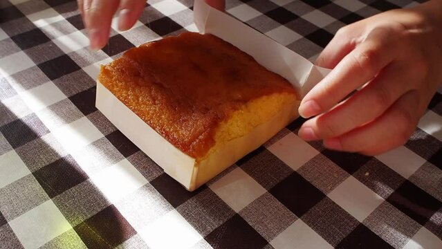 Traditional sponge cake, Sobao Pasiego. Typical spanish bake from Cantabria gastronomy. Sweet buttery muffin. Female hands removing baking paper on top of square pattern oilcloth. Cut in portions.
