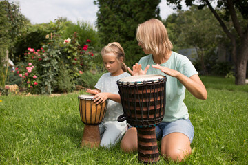 mom and child daughter play at ethnic drums sitting on the grass on a sunny day. a family hobby....