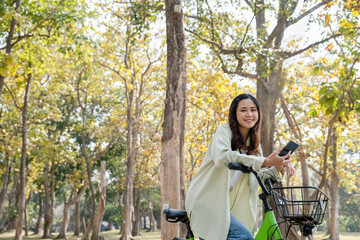 Happy woman riding bicycle and using phone at park.