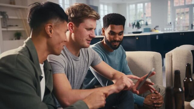 Group of male friends sitting on sofa at home looking at dating app on mobile phone together - shot in slow motion