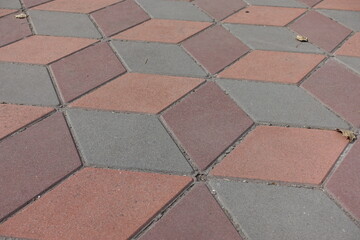 Surface of geometric pavement made of grey, coral red and maroon concrete tiles