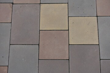 Surface of pavement made of pink, yellow, brown and grey concrete blocks