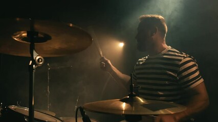 Male drummer plays a drum kit in a dark room full of smoke. Music or song recording, creation. Music band repetition