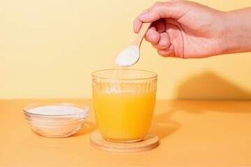 Person's Hand Adding Collagen Powder to Orange Juice