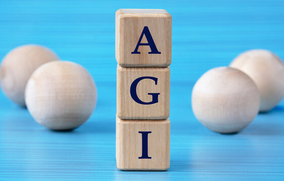 AGI - acronym on wooden cubes on a blue background with wooden round balls