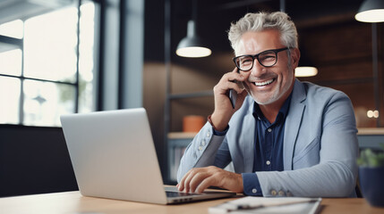 Happy senior businessman with laptop computer and smartphone in office