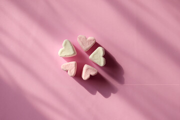 Delicate pink and white marshmallows in the shape of a heart on a pink background with copy space. Group of hearts marshmallow sweets placed in the center. Valentine's Day symbols tender marshmallow.