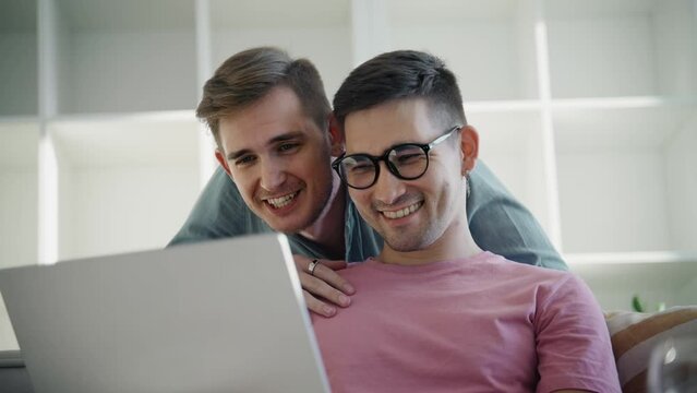 A young multiracial gay couple makes online purchases on a laptop after moving into a new apartment.