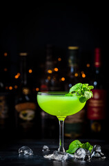 Last word green cocktail drink with dry gin, herbal liqueur, lime juice, mint and ice. Black bar counter background, steel bar tools and bottles