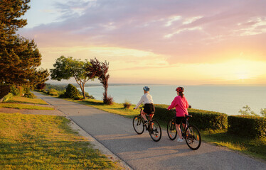 Two women riding on bicycle on the sea promenade. Back view.