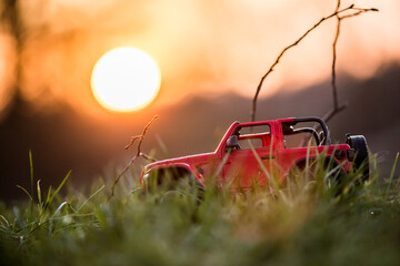 red off-road car in the grass against the background of the setting sun - obrazy, fototapety, plakaty