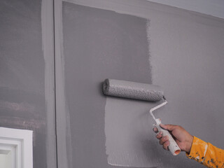 A worker is painting the walls of the house with a primer using a paint roller.