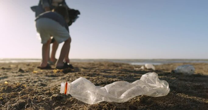 Volunteers mom and son collect plastic garbage on beach. Eco activists collects garbage on beach with garbage bag. Garbage collection on beach. Eco agenda, reasonable consumption, harm from plastic