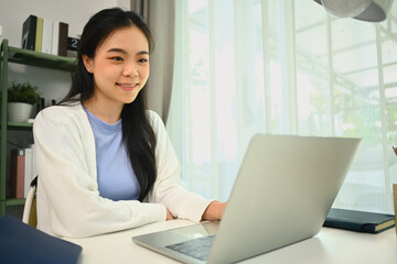 Satisfied Asian female freelancer searching information, working on laptop computer at home