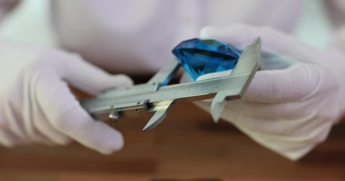 Measuring large blue diamond in hands of gemologist. Worker measures diameter of gemstones on jewelry scale