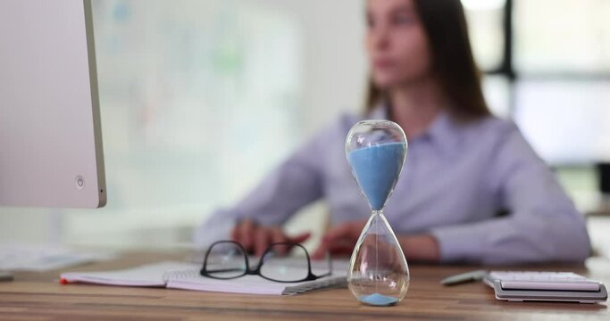 Hourglass closeup with employee human hands typing on computer. Hourglass with running sand on desktop and business, time management and deadline