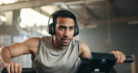 Papier Peint photo Fitness Asian man, headphones and cycling at gym on machine and listening to music in sports workout or exercise. Serious male person or athlete training on bicycle machine or equipment for healthy cardio