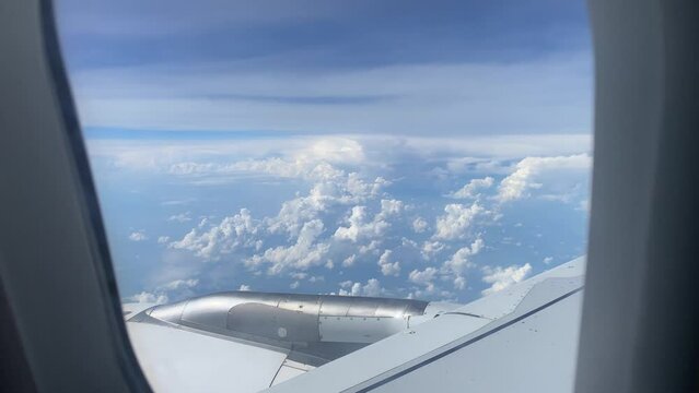Wing of flying over ocean and island airplane from window on clouds in blue cloudy sky. Aircraft wing in sunny weather in tropics. Passenger jet flight. Travel, tourism, journey, trip, wanderlust.
