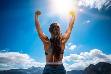 Deurstickers Vista trasera de una mujer deportista en la cima de una montaña con los brazos alzados a un nuevo día de éxito y superación.Concepto de crecimiento personal y desarrollo. © TaniaC.