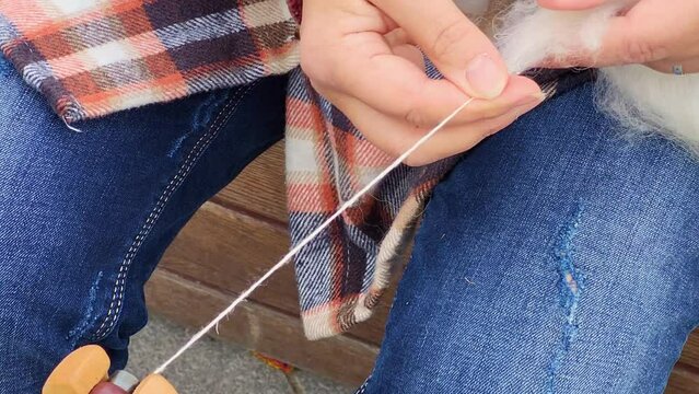 The woman is spinning wool on a wooden spinning wheel. Close-up of a woman's hands knitting wool
