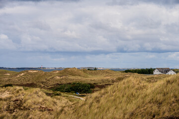 Dramatische Wolken im D&uuml;nenbereich der Nordseeinsel Amrum der Blick geht hin&uuml;ber zur Nachbarinsel Sylt mit dem Leuchtturm von H&ouml;rnum