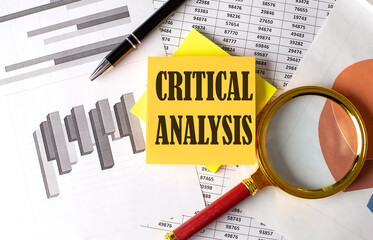 CRITICAL ANALYSIS text on a sticky on the graph background with pen and magnifier