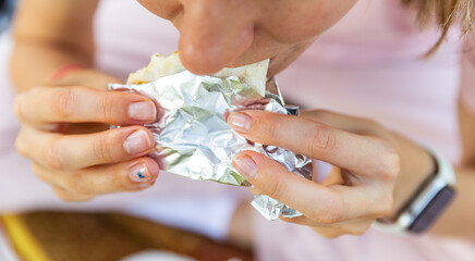 Close up of mouth eating food in public. Hungry woman bites a big pita or shawarma outdoor.