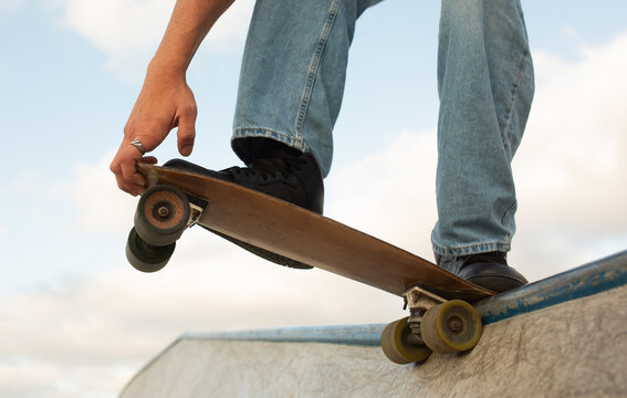 Unrecognizable young sports guy skateboarder riding at skate park with concrete walls, doing ramp tricks, closeup