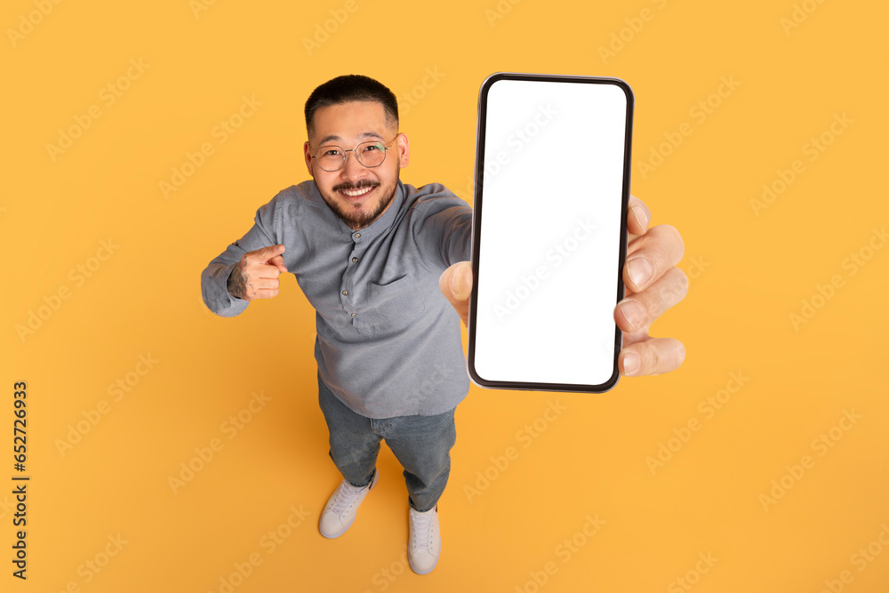 Poster check this. smiling asian man pointing at big blank smartphone in hand