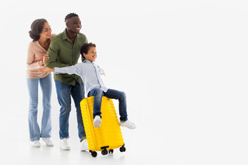 Joyful Diverse Parents Riding Son On Travel Suitcase, White Background