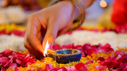 Closeup shot of lighting up an oil lamp placed in the center of a Rangoli - Diwali festival  Diwali diy. Female decorating a floral Rangoli with a colorful Diya - a Hindu festival  auspicious occas...