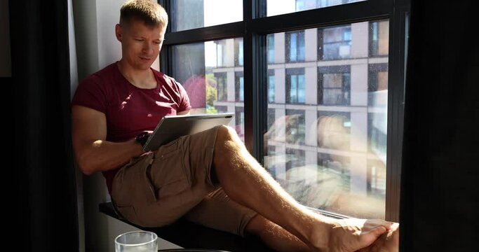 Business man sitting and holding tablet. Successful man with thinking expression working at home near window