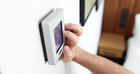 Person regulates air temperature in room at home or in office using remote control on wall. Climate control concept
