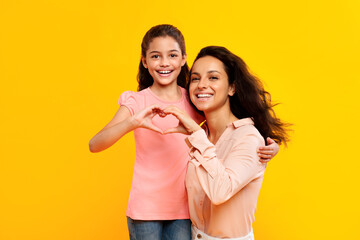 Smiling european mother and daughter showing heart symbol with fingers, connecting their hands together and smiling