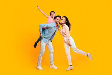 Full body length of happy mother, father and daughter laughing, dad carrying girl on back