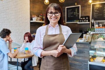 Portrait of a middle aged woman owner or worker of coffee shop, inside a bakery