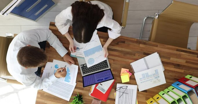 Analyst team uses documents to analyze and specify office paper analysis report. Business people studying report on table to understand business top view