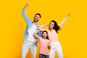Victory concept. Overjoyed european family of three shaking clenched fists, making winner gesture over yellow background - obrazy, fototapety, plakaty
