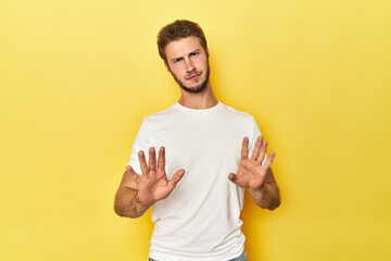 Young Caucasian man on a yellow studio background rejecting someone showing a gesture of disgust.